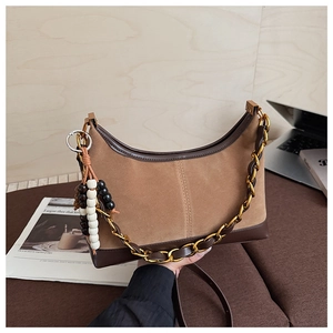 Detail of brown suede hobo bag with chunky gold chain and beaded charm on office desk