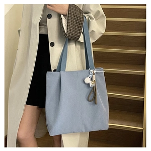 Detail view of light blue canvas tote bag with pompom charm on a casual outfit
