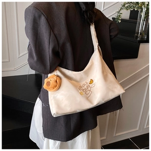 Detail of off-white tote bag with brown letter embroidery and plush bear pendant accessory