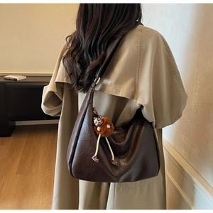 Detail of dark brown matte leather shoulder bag with a cute plush doll charm