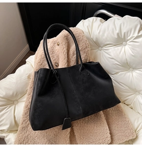 Detail shot of black suede tote bag with slim shoulder straps on a textured fabric