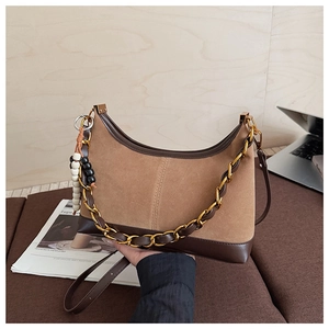 Detail of suede crescent bag with gold chain and wooden bead charm in a warm aesthetic