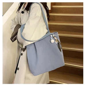 Detail view of large blue canvas tote bag with white fluffy charm on a side shoulder strap