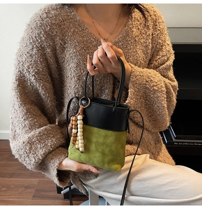 Detail of green quilted suede bucket bag with contrast black trim and wooden bead charm