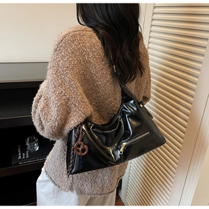 Détail du sac hobo noir brillant avec finitions dorées et breloque bretzel créative