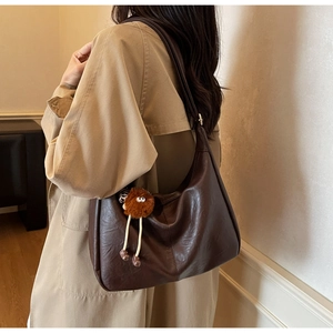 Brown leather hobo bag with plush charm shown on model in a minimalist setting