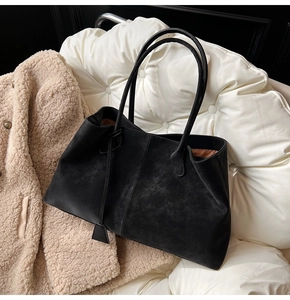 Close-up of black suede tote bag texture with elegant pendant on white quilted surface