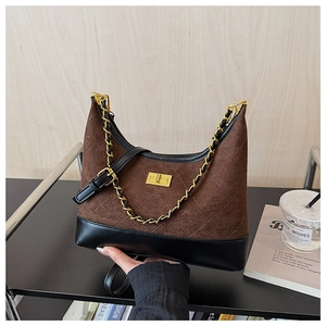 Detail of quilted suede crossbody bag with golden twist lock and chain strap on a display shelf