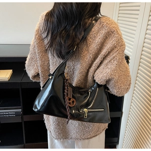 Détail d'un sac hobo noir brillant avec fermeture éclair et charm tressé marron décoratif