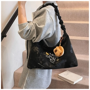 Detail of black pleated bag with cursive embroidery, star charms and plush bear pendant