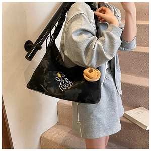 Detail of black pleated tote bag with embroidery, brown plush charm and soft fabric texture