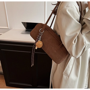 Nahaufnahme der braunen Wildleder-Baguette-Tasche mit Kekshänger auf der Schulter