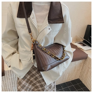 Détail du sac bandoulière en daim tressé marron foncé avec chaîne dorée et breloque