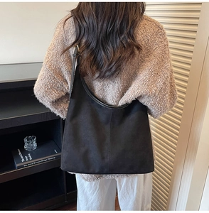 Detail of black suede hobo bag styled with a chunky knit sweater and white trousers