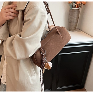 Nahaufnahme der braunen Wildleder-Achseltasche mit Baseball-Anhänger und Lederriemen