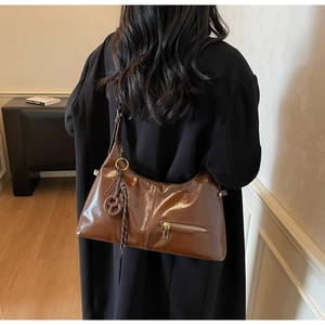Détail du sac en cuir marron brillant avec anneau latéral et pendentif tissé chic