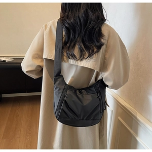 Detail of black crescent crossbody bag with pleats and brand tag on a neutral trench coat