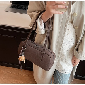 Detail einer braunen Wildleder-Baguette-Tasche mit Reißverschluss und Baseball-Anhänger