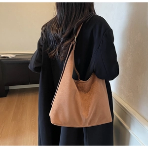 Detail of a large brown suede hobo bag worn over a black blazer for a retro look