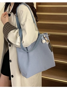 Light blue canvas tote bag with woven strap and plush charm shown on a female model