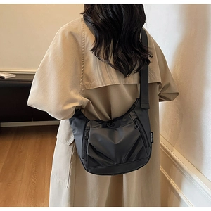 Rear view of a black nylon hobo crossbody bag worn with a beige coat in a cozy room