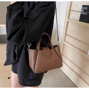 Detail of premium brown pebble leather handbag with round buckle and adjustable strap