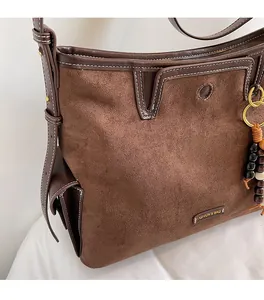 Detailed close-up of brown suede bag with white stitching and wood bead charm