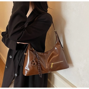 Gros plan d'un sac hobo en cuir marron brillant avec nœud décoratif et breloque