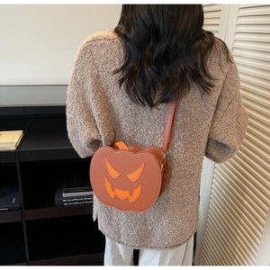 Detailed close-up of a pumpkin-shaped Halloween shoulder bag with a black ghost face design