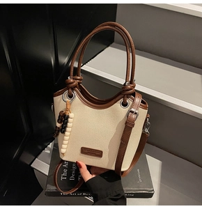 Détail du sac seau en toile montrant le logo en cuir et le pompon en perles de bois