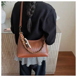 Detail of vintage brown crossbody bag with metal chain and wooden bead charm on a model