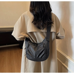 Back view of a dark grey crescent nylon crossbody bag on a model in a trench coat