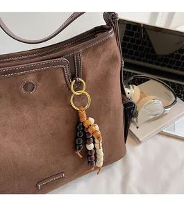 Detailed view of brown suede tote bag with wooden bead charms and metal logo plaque