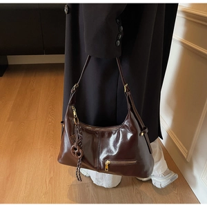 Détail du sac hobo en cuir poli marron foncé avec ferrures dorées et breloque nouée
