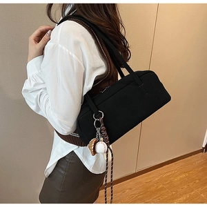 Detail einer schwarzen Baguette-Tasche mit Baseball-Anhänger und Schulterriemen