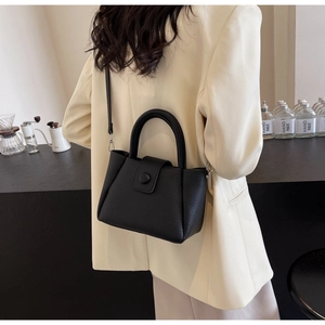 Detail of a black pebbled leather bucket bag styled with a cream blazer in a cafe setting