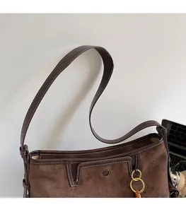 Detail of suede shoulder bag featuring contrast stitching and gold metal ring hardware