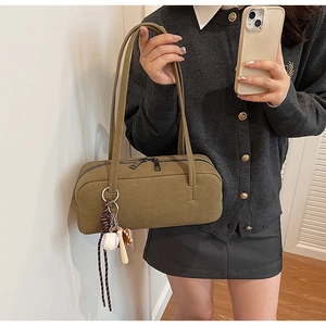 Detailansicht der olivgrünen Wildleder-Baguette-Tasche mit Baseball-Anhänger und Riemen