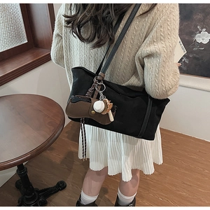 Detail of black canvas tote bag with brown leather straps and baseball charm