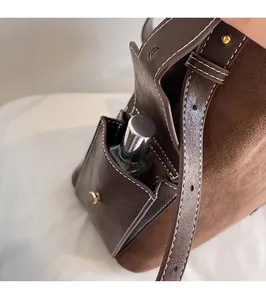 Close-up of suede shoulder bag side pocket with white stitching and gold metal buckle