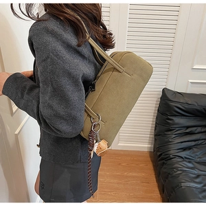Olivgrüne Canvas-Schultertasche mit Baseball-Anhänger in harmonischer Lifestyle-Szene