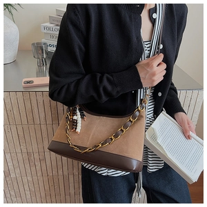 Detail of suede crossbody bag featuring gold chain strap and beaded tassel pendant