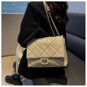 Close-up of a quilted beige leather crossbody bag with a golden chain strap and clasp