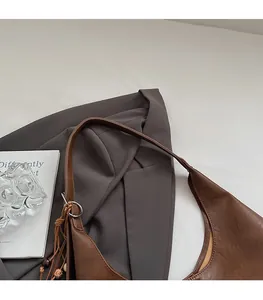 Detail of a brown leather shoulder bag featuring a decorative fringe and wood bead charm