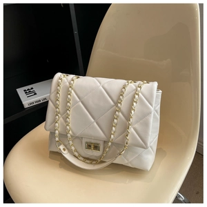Detail of white quilted leather bag with gold chain strap on a modern chair