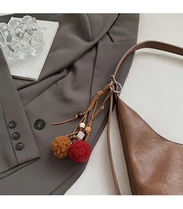 Detail of red and brown plush ball pendant with wooden beads on a leather bucket bag