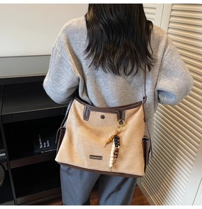 Detail of a beige suede tote bag with brown leather trim and colorful wooden bead charm