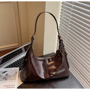 Vue détaillée du sac hobo en cuir brillant marron foncé avec fermetures éclair sur un bureau