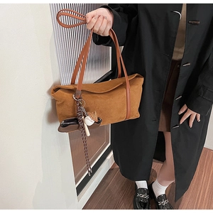Détail d'un sac cabas en daim marron avec bandoulière en cuir et pendentif de baseball décoratif