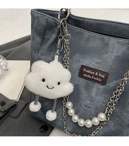 Nahaufnahme von weißem Plüschwolken-Anhänger mit Perlenkette an blauer Jeans-Tasche